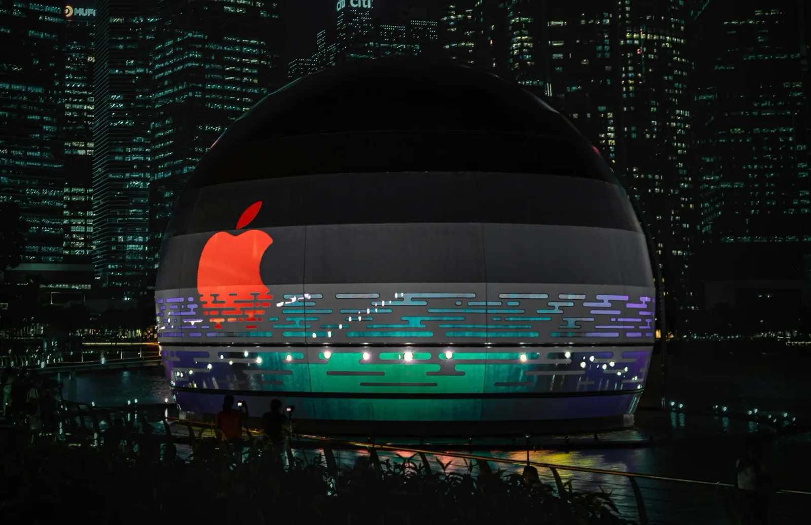The floating Apple store at Marina Bay Sands lit at night, its dome carrying a red Apple logo against the Singapore skyline