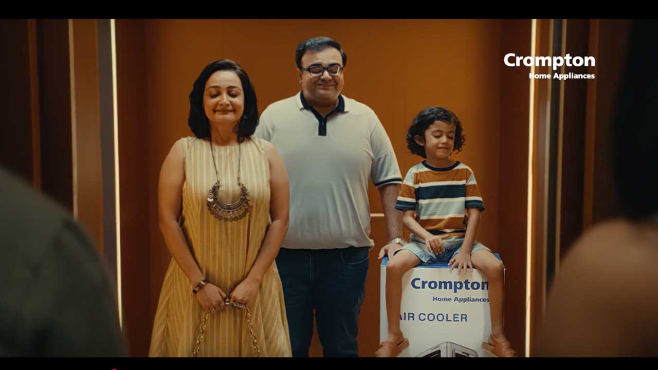 A family standing in a lift with a boxed Crompton air cooler, from the campaign film