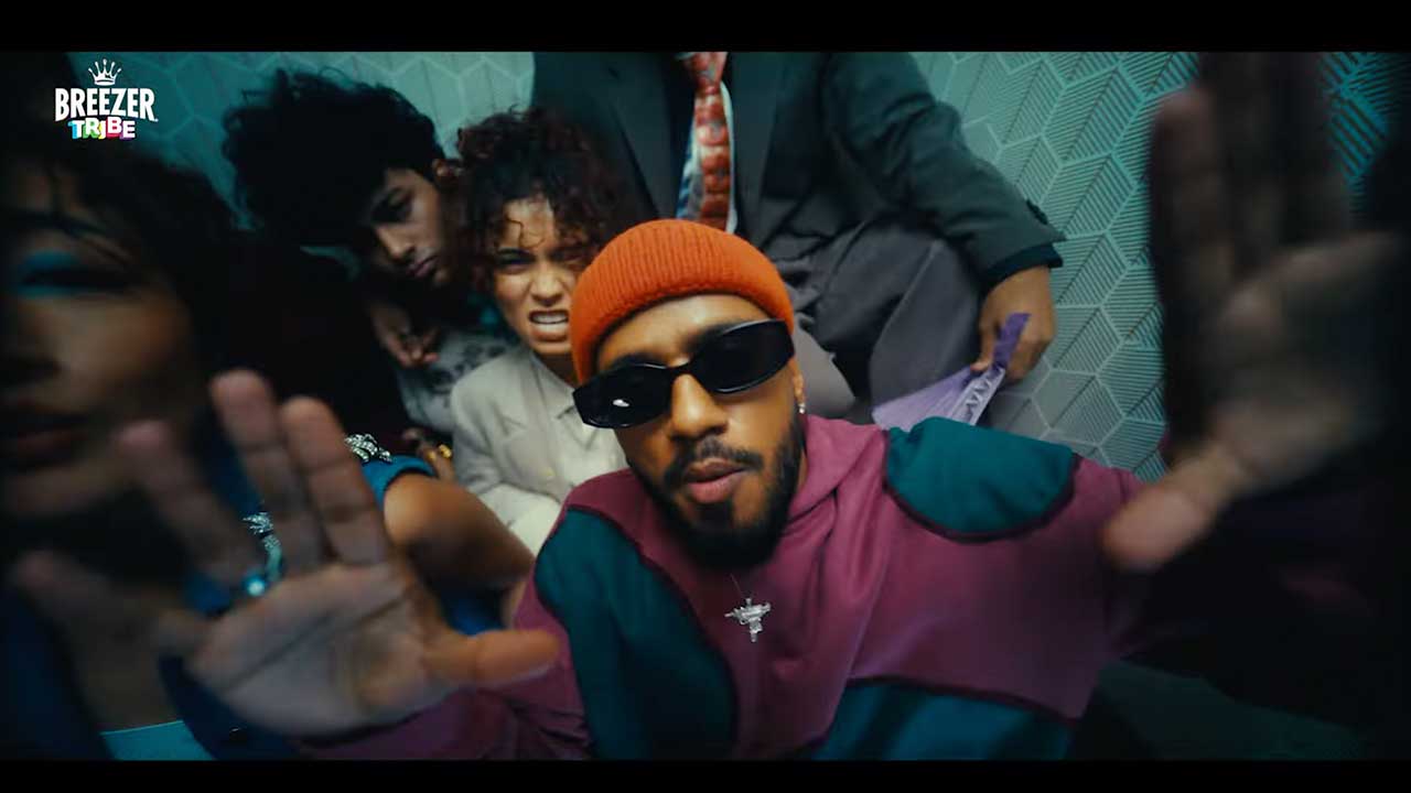 A rapper in an orange beanie and dark glasses fronting a crowd, from the BREEZER Tribe film
